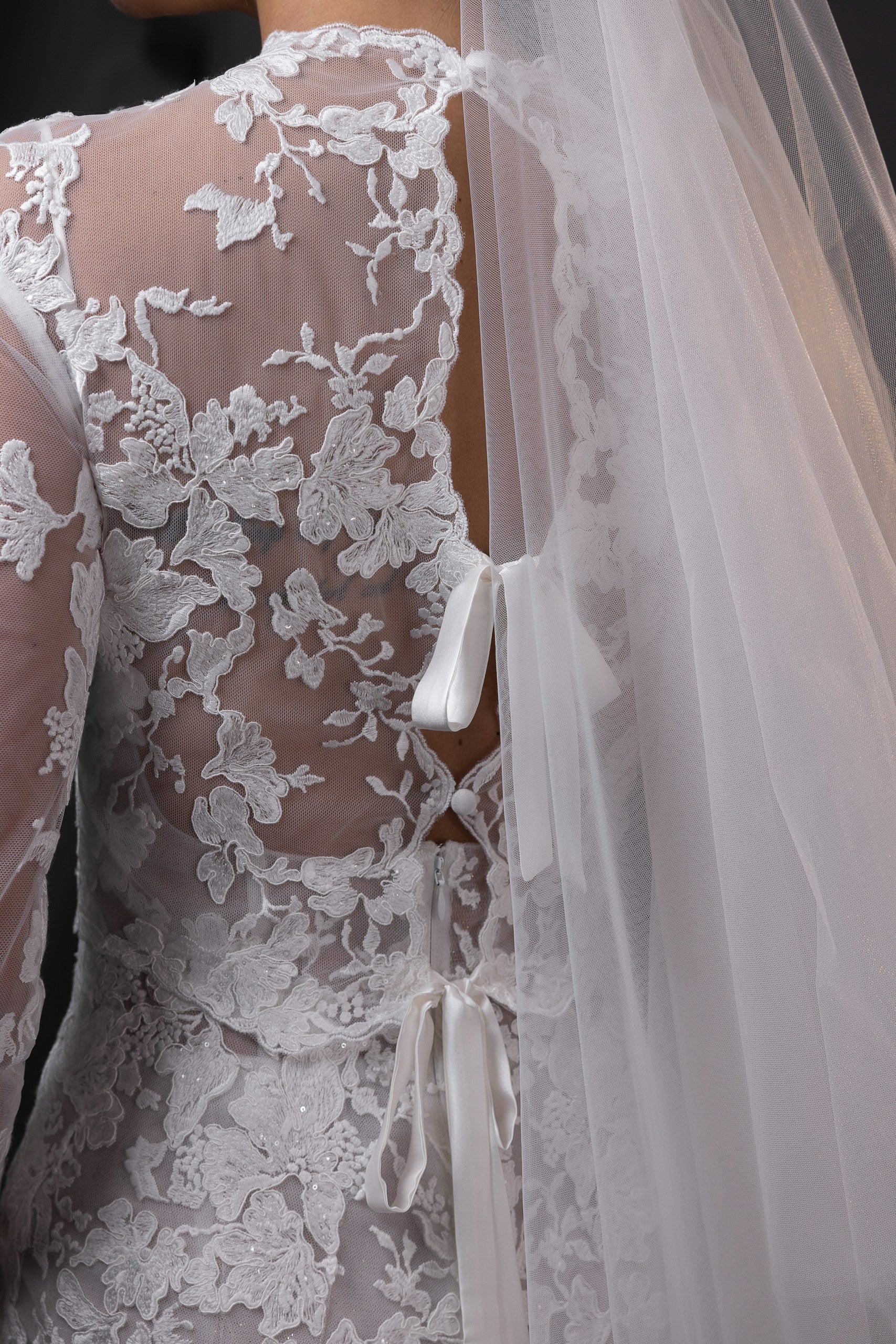 Michelle lace bridal topper with long sleeves, illusion neckline, and silk charmeuse bows, styled with a veil in Toronto.